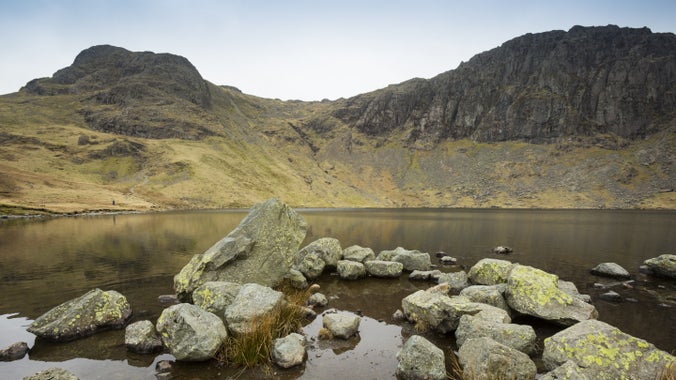 View of the rock-strewn lake at Stickle tarn with mountains rising above it and reflecting in the water